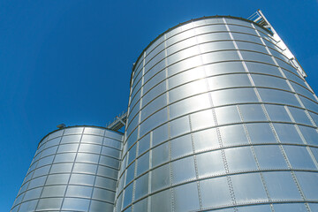 silver silos on agro manufacturing plant for processing drying cleaning and storage of agricultural products, flour, cereals and grain. Large iron barrels of grain. Granary elevator
