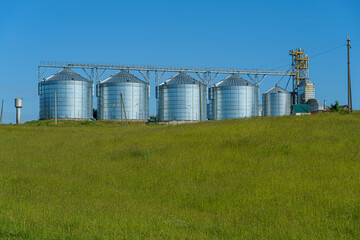 silver silos on agro manufacturing plant for processing drying cleaning and storage of agricultural products, flour, cereals and grain. Large iron barrels of grain. Granary elevator