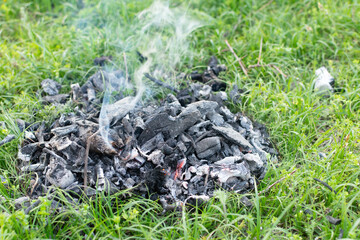 smoldering coals from a fire on the grass and smoke