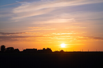 Beautiful sunset over the Dutch countryside. Silhouette of power lines and farm against the colorful evening sky.