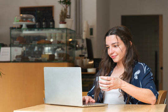 Woman enjoys coffee while working on laptop in cafe