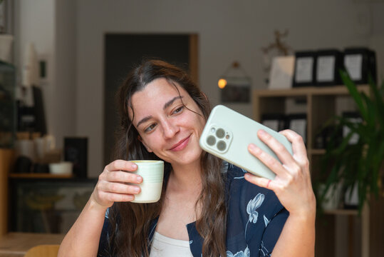 Woman enjoys coffee while taking a selfie with smartphone