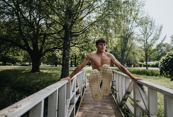 A shirtless man executing a dynamic parkour jump on a bridge in a sunny park, surrounded by lush...