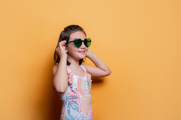 Young girl in sunglasses and swimwear against yellow background