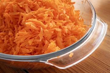 A glass dish with fresh grated carrots. Grated ingredient for salad, meat or baking. Product with...