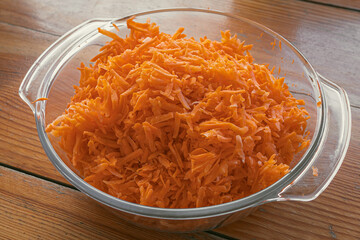 A glass dish with fresh grated carrots. Grated ingredient for salad, meat or baking. Product with vitamin A. Dietary nutrition. Vegetable diet. Vegetarian menu. Cheerful orange color.