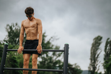 Athletic man performing pull ups on a bar in an outdoor park, focusing on biceps, lateral muscles, and shoulders.