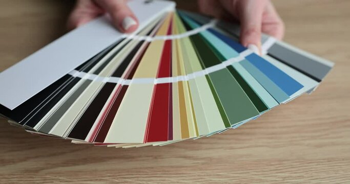 Multi-colored palette opened by hands of woman above wooden table. Different color variations for stylish interior design and house renovation