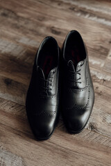 Two black dress shoes with red laces are standing on a wooden floor. The shoes are well-polished and appear to be made of leather. Concept of elegance and sophistication