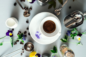 Cup with hot espresso and coffee bean and barista tools on white table.