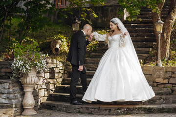 A bride and groom are walking down a stone staircase. The bride is wearing a white dress and the groom is wearing a suit. The scene is set in a garden with potted plants and a vase