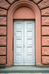 Large gray double doors with square patterns in an arched entryway, leading to the outside world