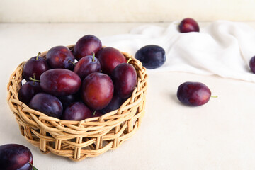 Wicker bowl with fresh ripe plums on white background