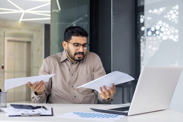 Stressed businessman confused with paperwork at office desk
