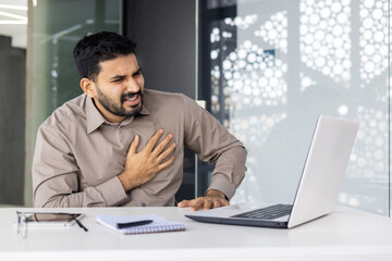Businessman experiences chest pain while working on laptop in office. Health and stress in the...