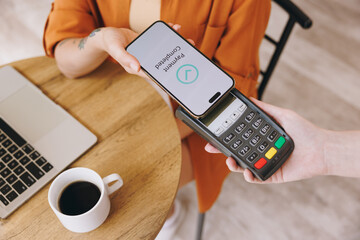 Cropped young woman hold bank payment terminal to process acquire mobile cell phone pay bill sits...