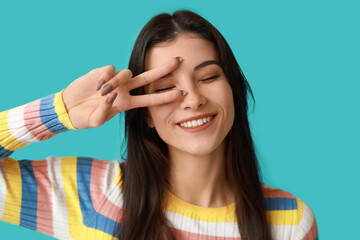 Young woman showing peace sign on blue background, closeup