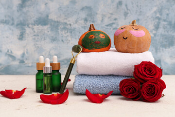 Pumpkins with drawn faces, spa supplies, roses and clay mask on white table