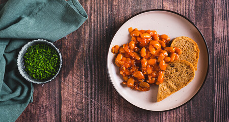 Plate with baked beans in tomato sauce and rye bread on the table top view web banner