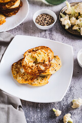 Homemade cauliflower fritters on a plate and sour cream in a bowl on the table vertical view