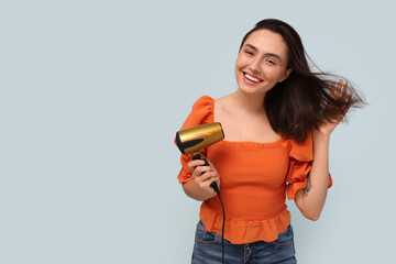Beautiful young woman with hair dryer on light background