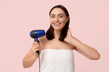 Beautiful young woman with hair dryer on pink  background