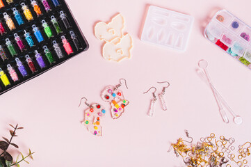 Earrings made of epoxy resin, molds and sparkles for making on a pink background top view