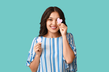 Beautiful young Asian woman with pink paper hearts on blue background. Valentine's Day celebration