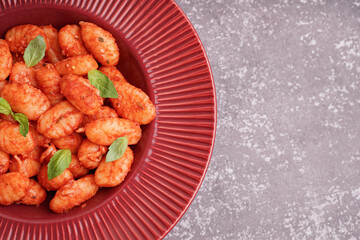 Plate of tasty gnocchi with tomato sauce on grey background