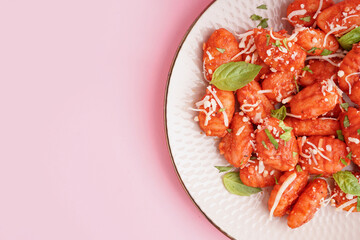 Plate of tasty gnocchi with cheese on pink background