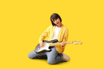 Cool young woman playing electric guitar on yellow background
