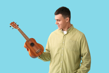Handsome young man with ukulele on blue background
