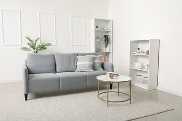 Interior of light living room with grey sofa, table and shelf units