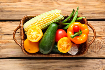 Wicker basket with different fresh vegetables on wooden background