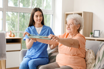 Young nurse and senior woman with stretching band training at home