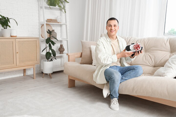 Obraz premium Young man with gift VR glasses sitting on sofa at home