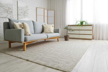 Interior of stylish living room with comfortable sofa, folding screen, chest of drawers and carpet