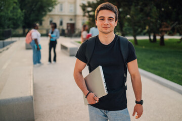Young exchange student boy with laptop at campus looking at camera.