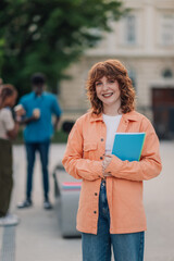 Happy college girl with textbook at campus posing and smiling at camera