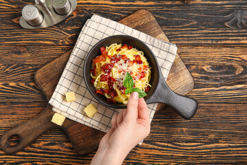 Woman decorating tasty pasta carbonara with basil on wooden background