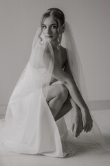 A woman in a white dress is posing for a photo with a veil. She is wearing a ring and a necklace
