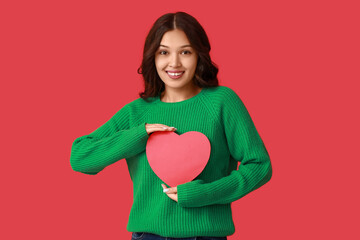 Beautiful young Asian woman with red paper heart on color background. Valentine's Day celebration