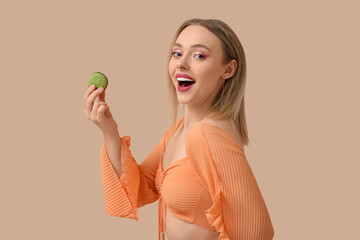 Happy young woman with green sweet macaroon on beige background