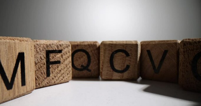 Circle made up of wooden cubes with letters of English alphabet. Blocks with letters stand in random order on white table surface in studio