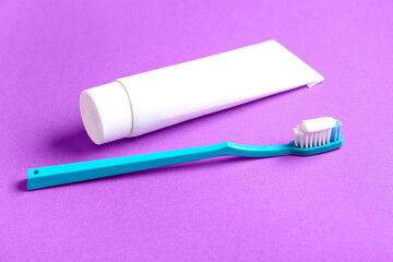 Tube of tooth paste and blue brush on purple background