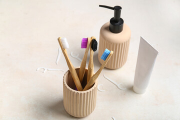 Cup with toothbrushes, tube of toothpaste and soap dispenser on beige grunge background