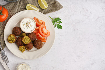 Plate with delicious falafel balls, lime, sauce and tomatoes on light background