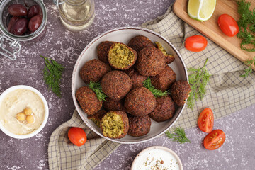Bowl with delicious falafel balls, tomatoes, hummus and olives on grunge background