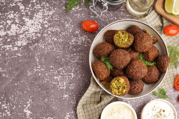 Bowl with delicious falafel balls, sauces and tomatoes on grunge background