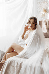 A woman in a white gown is sitting on a bed